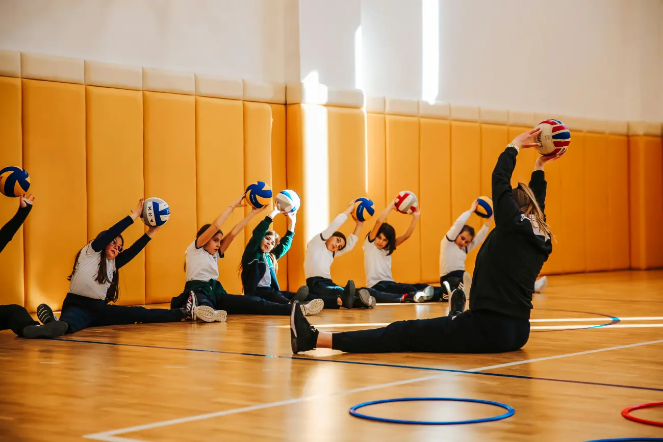 Students and teacher sat on the floor with a ball over there head.