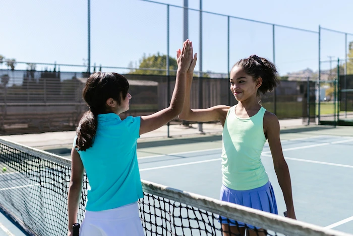 Children high fiving across a tennis court net.